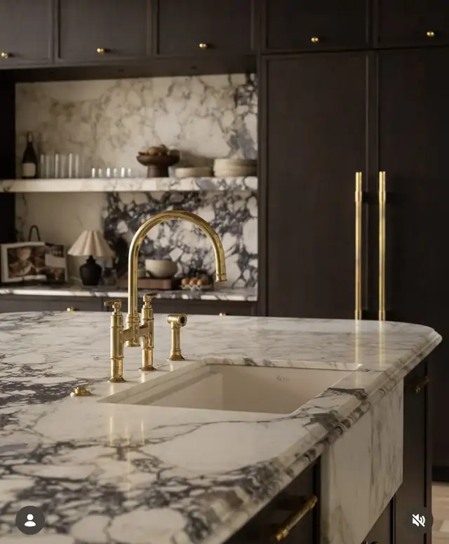 Kitchen detail with a white and violet veined marble counter, brass bridge faucet and dark cabinetry with brass pulls
