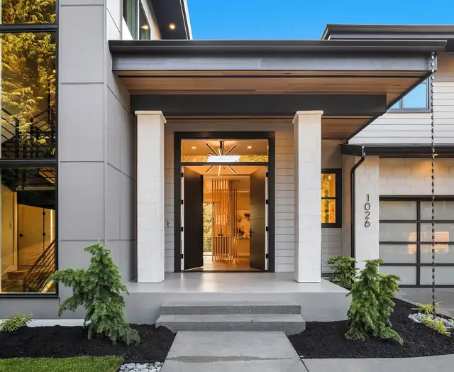 Front entry of a new modern home with a covered porch, glass double doors and warm interior lighting