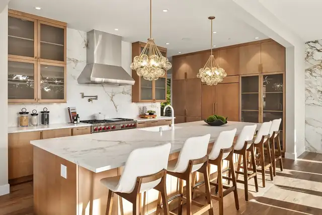 Kitchen by ARIID with walnut cabinets, a marble island with white counter stools, crystal pendant lights and a stainless range hood