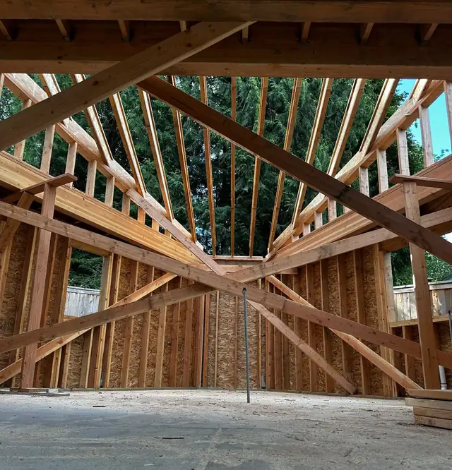New construction framing with exposed wood studs, beams and roof rafters over a concrete slab