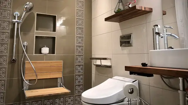 Accessible bathroom remodel with a fold-down teak shower seat, handheld shower on a slide bar, tiled niches and a floating wood shelf