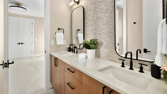 Bathroom with a walnut vanity, white stone top, matte black faucets and an arched black mirror