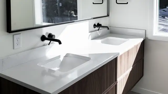 Bathroom remodel with a white stone double vanity, wall-mounted black faucets, wood cabinet base and large black-framed mirror