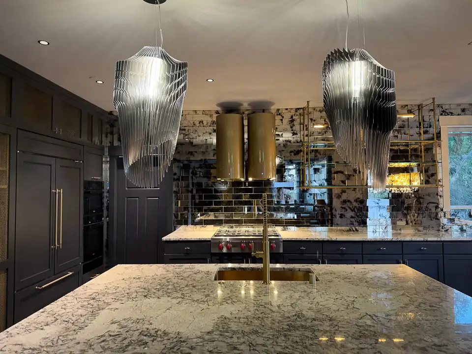 Design-build remodeling Kirkland WA: dark-cabinet kitchen with a granite island, brass faucet, mirrored backsplash and sculpted glass pendants