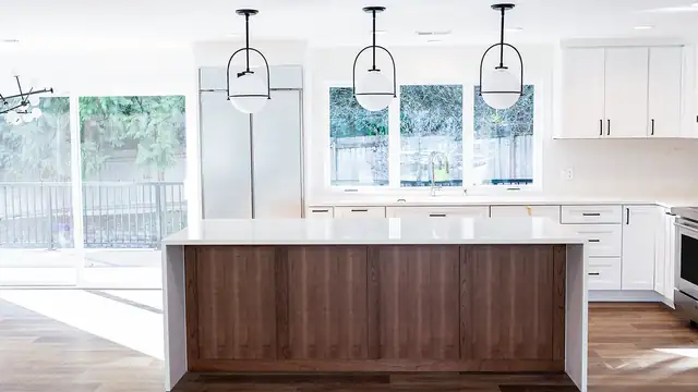 Bright white kitchen with a walnut island, quartz top, three pendant lights and sliding doors to the yard