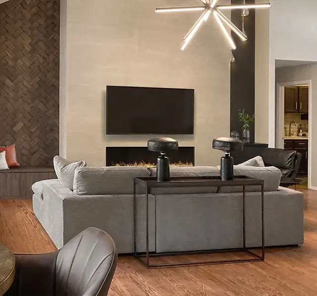 Remodeled living room with a linear gas fireplace in a tall tile wall, gray sectional sofa and starburst light fixture